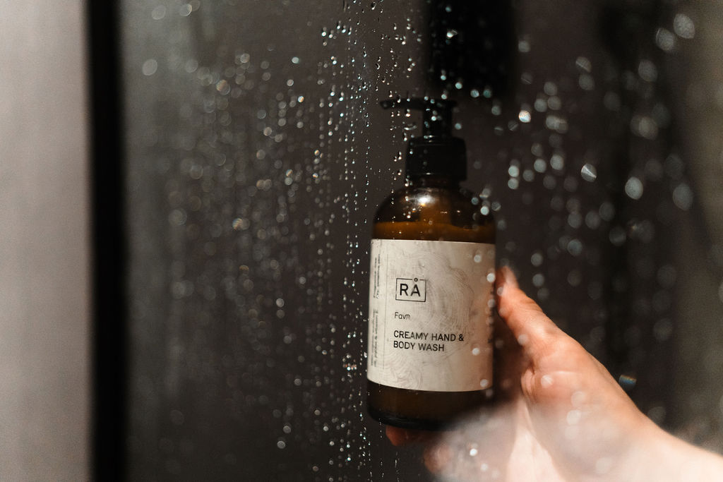 favn creamy hand and body wash holdes av en hånd under rennende vann i dusjen