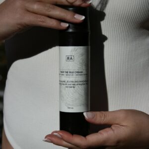 Dame med hvit badedrakt holder favn the silk cream innill magen for å vise at kremen er fin etter sol og bading