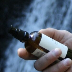 Holder rå skincare olje i hånden med norsk natur og foss i bakgrunnen