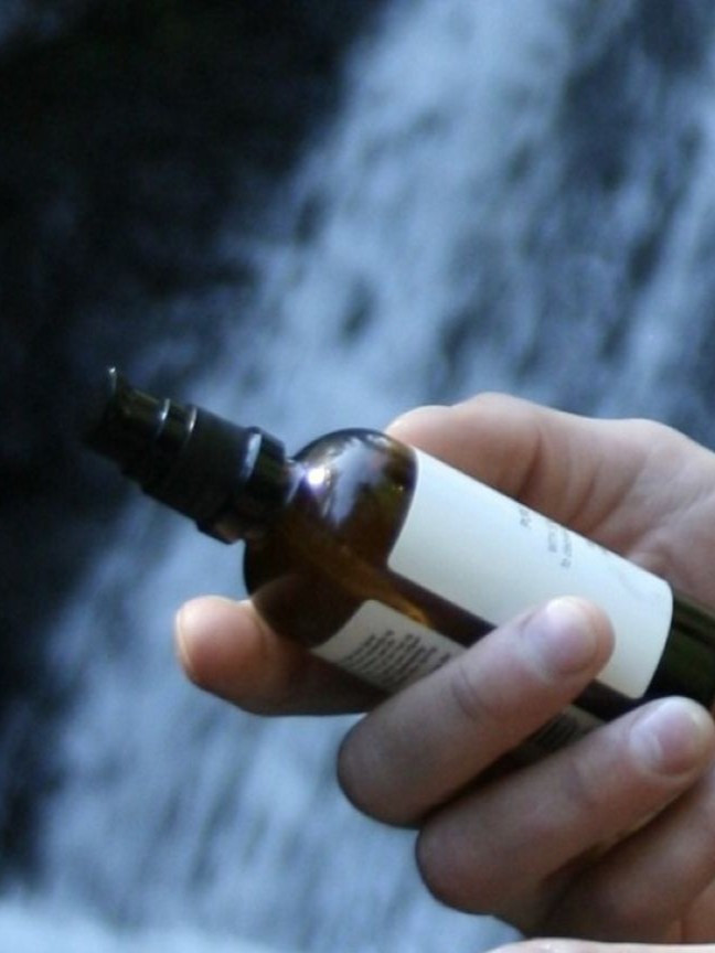 Holder rå skincare olje i hånden med norsk natur og foss i bakgrunnen