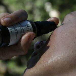 Person påfører RÅ Correcting Serum med vitamin C og bakuchiol på ansiktet utendørs.