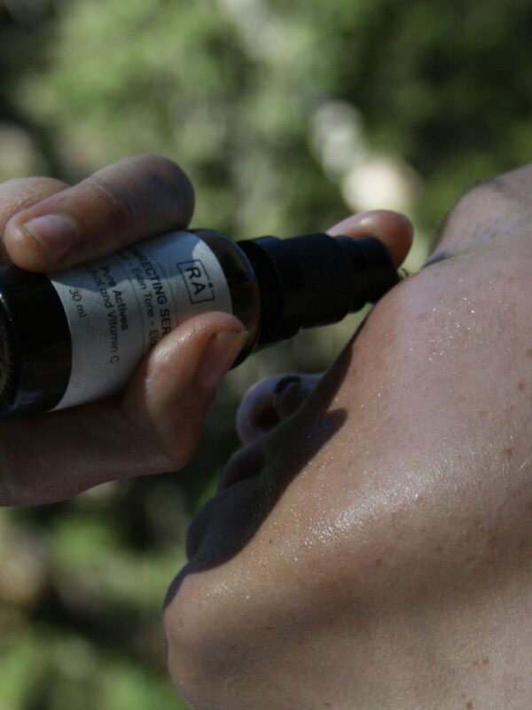 Person påfører RÅ Correcting Serum med vitamin C og bakuchiol på ansiktet utendørs.