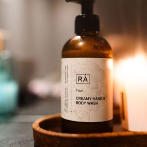 RÅ Favn Creamy Hand & Body Wash på et brett ved siden av et tent lys.