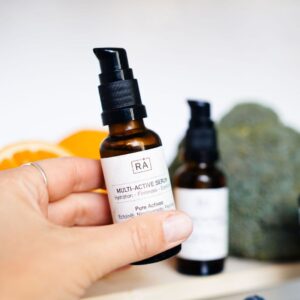 Multi-Active Serum from RÅ Skincare is held in the hand in front of fresh blueberries, fruit and green ingredients.