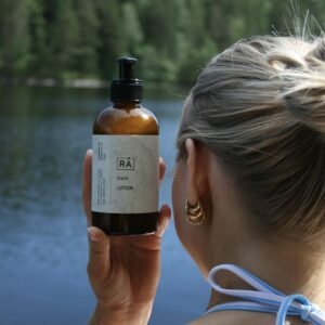Grøde lotion holdes opp av dame som sitter på bryggen en sommerdag