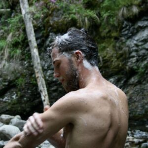 mann står ute i naturen og vasker kroppen sin med grøde såpe fra norske rå skincare. I bakgrunnen ser du et fjell med mose på