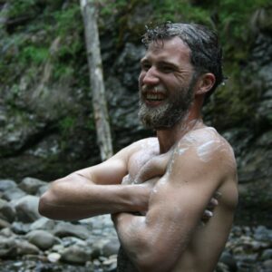 mann vasker kroppen med sevje såpe med skogsduft fra norske Rå skincare. Han står ute med skogen i bakgrunnen