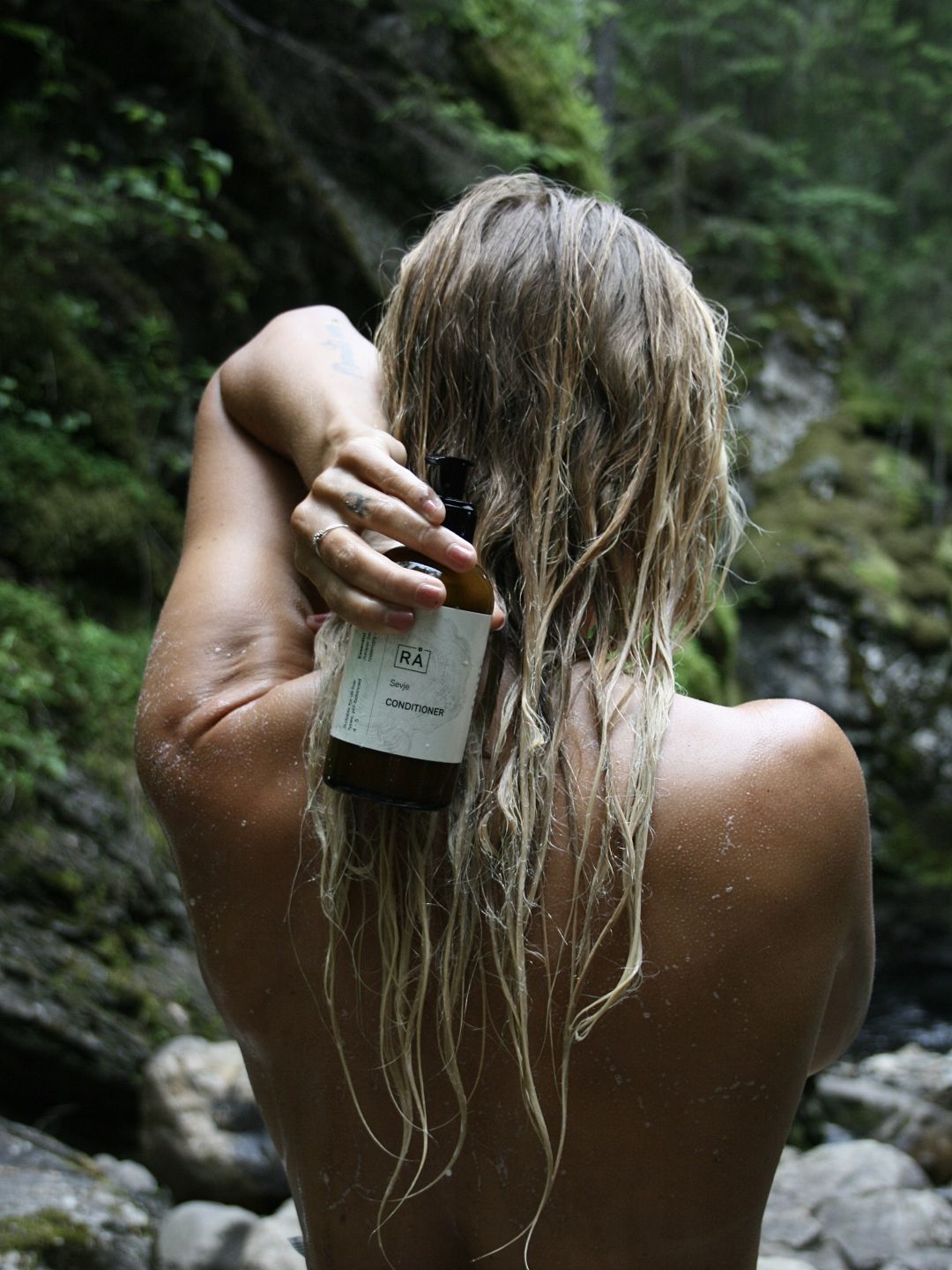 Dame med vått hår og balsam i håret holder grøde balsam fra rå skincare forran håret