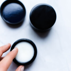 Sos ceramide balm. Krukken er åpen og en dame tar fingen oppi for å ta ut krem