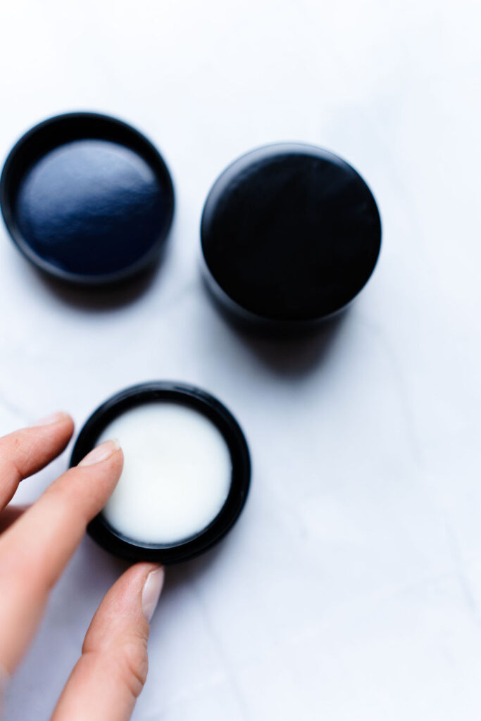 Sos ceramide balm. The jar is open and a woman puts her finger inside to take out the cream.