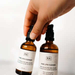 Pure lipid cleanser 50 ml og 100 ml vises sammen. En hånd holder reisestørrelsen på 50 ml.