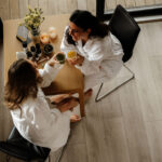 To damer skåler med smudi ved bordet. På bordet er det tapas og hudpleie fra RÅ Skincare