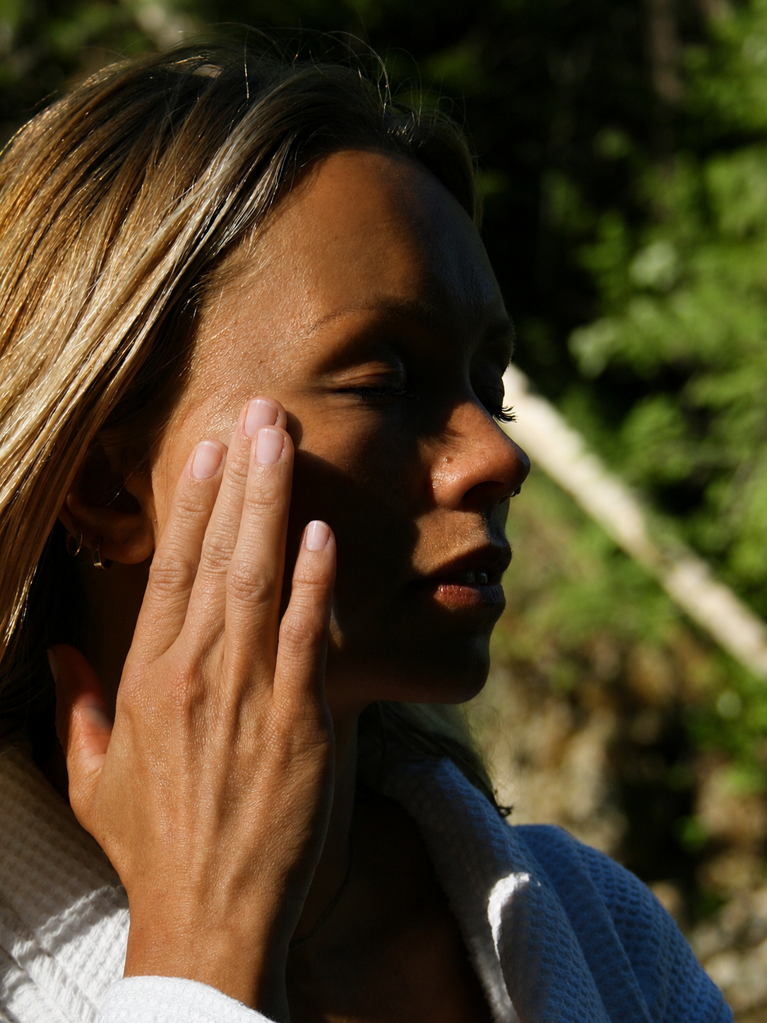 Dame smører rå skincare ansiktskrem på huden i naturen med skogen i bakgrunnen