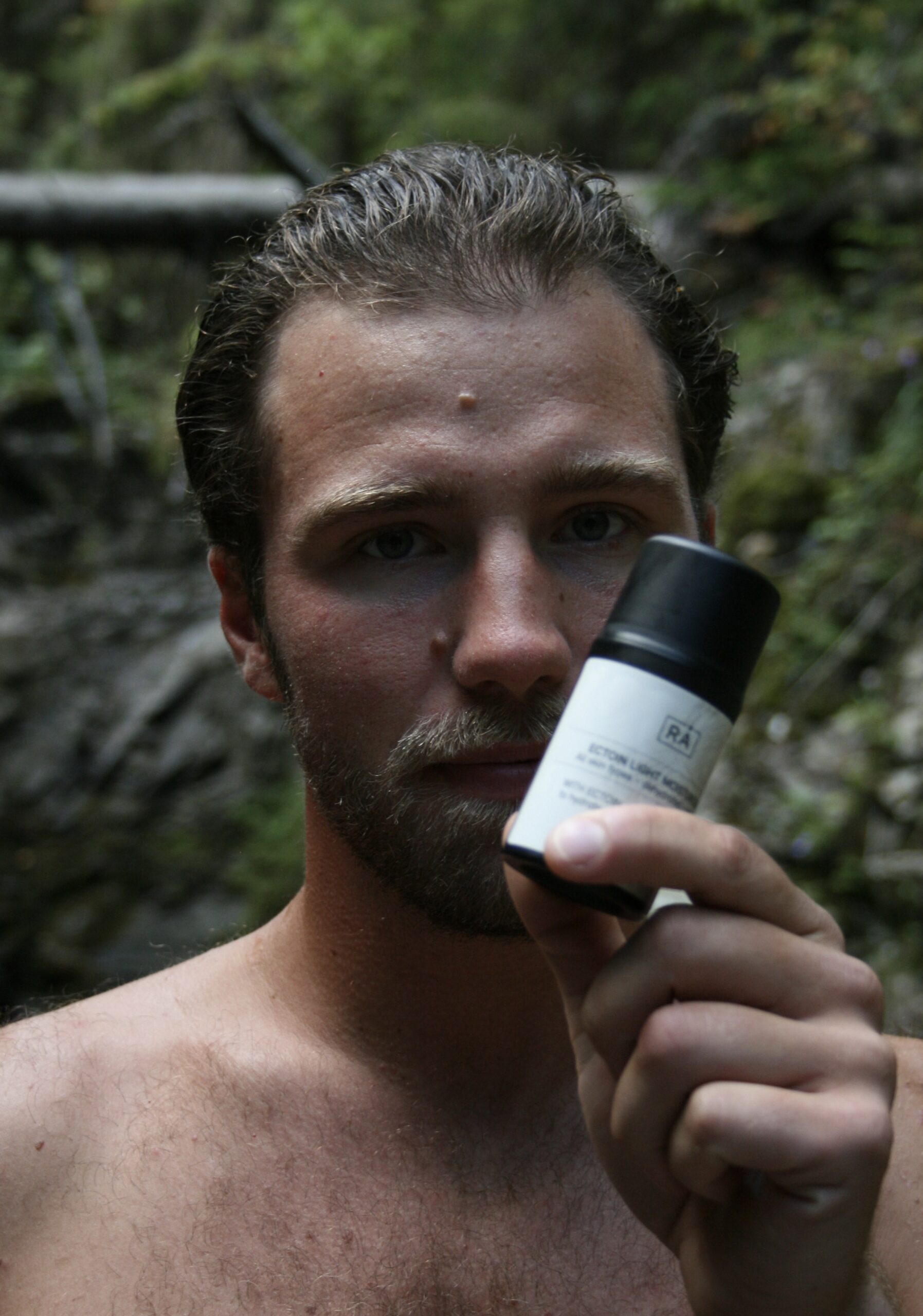 Mann holder rå skincare ectoin light moisturiser for sensitiv hud i hånden forran ansiktet