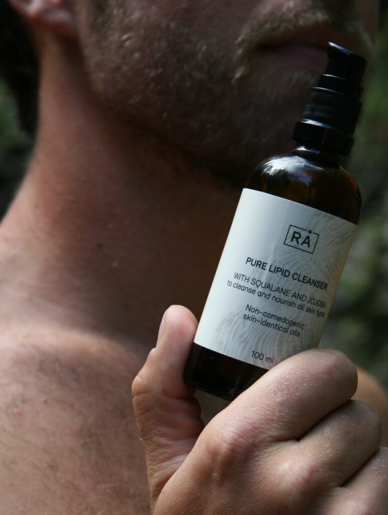 Nærbilde av mann holder RÅ pure lipid cleanser foran ansiktet.